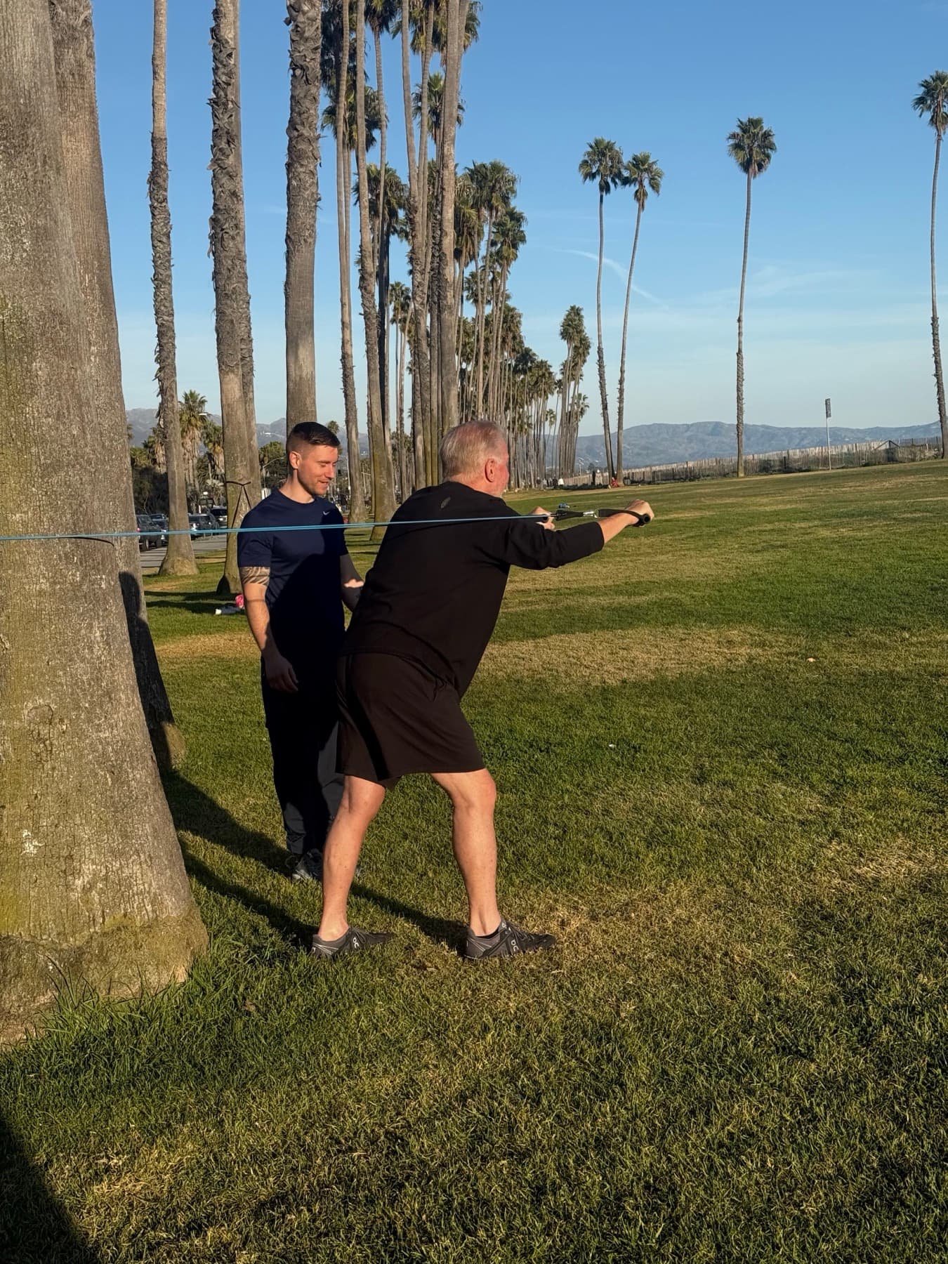 Laurence Larsen coaching a senior client through banded resistance training outdoors at a Santa Barbara park